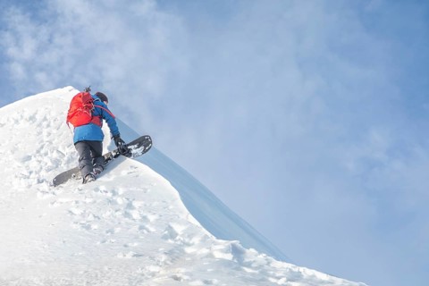 A skier with a red backpack ascends a snowy mountain, showcasing the adventurous spirit of ski