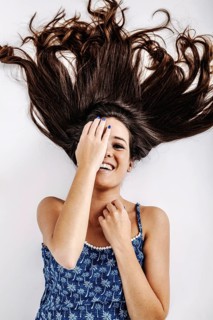 A young woman joyfully lies on the floor, her long hair spread out around her. She playfully covers