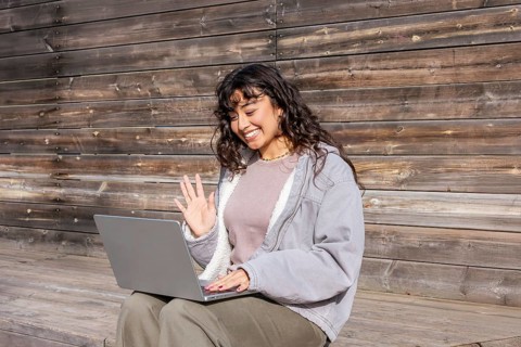 A young Latin woman enjoys a sunny day, sitting on a wooden bench and interacting with her laptop