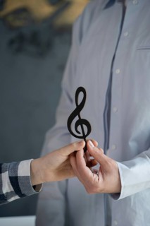 Close-up of two hands holding a wooden treble clef symbol, symbolizing collaboration and creativity
