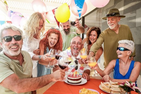 Joyful group of friends gathered around a table celebrating a birthday with a cake and drinks.