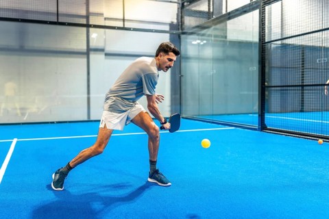 Male athlete on a blue indoor pickleball court intensely focused on hitting a yellow ball with his