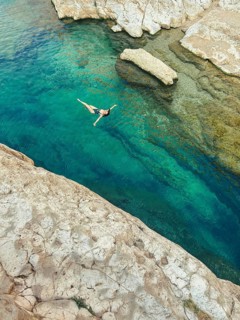 From above a woman is swimming into the vibrant turquoise waters of Wadi Ash Shab, oasis in Oman,