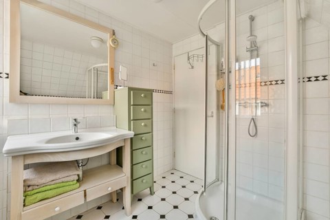 A sleek and modern bathroom featuring a shower, large mirror, and neatly organized storage. The