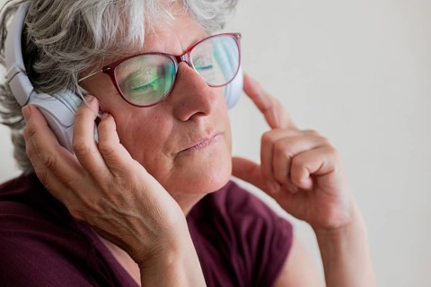 An elderly woman with glasses and headphones enjoys music intensely, closing her eyes for a moment