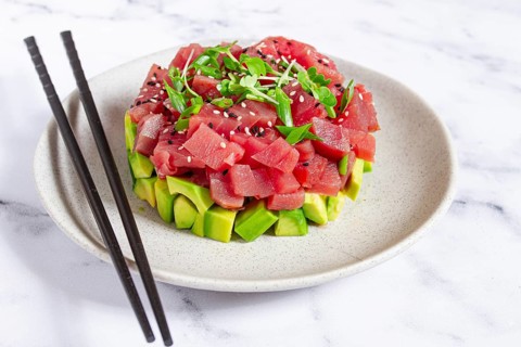 Fresh tuna tartare with avocado served on a marble table with soy sauce and seaweed salad
