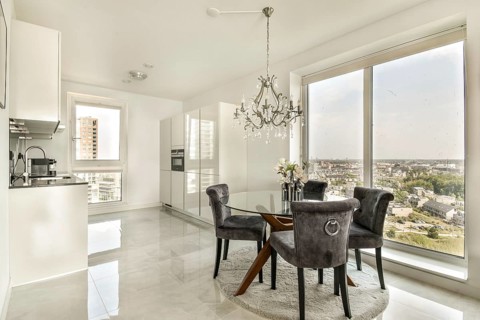 Elegant dining area with a chic glass table, plush chairs, and a stunning chandelier. Overlooks a