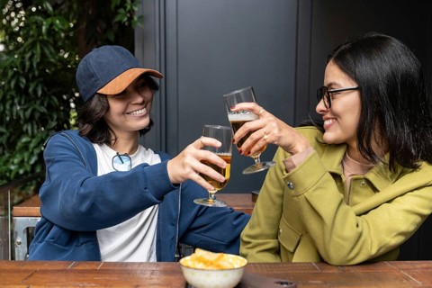 A joyful lesbian couple clinks glasses in an intimate setting, sharing laughter and good times.