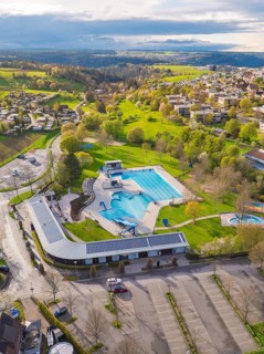 Urban view of an outdoor swimming pool with car park and surrounding green landscape, Calw