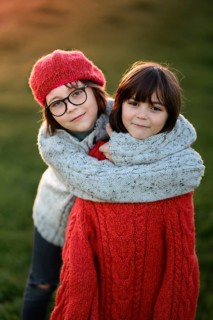 Two siblings, a boy and a girl, share a cozy embrace outdoors during an autumn sunset. The boy