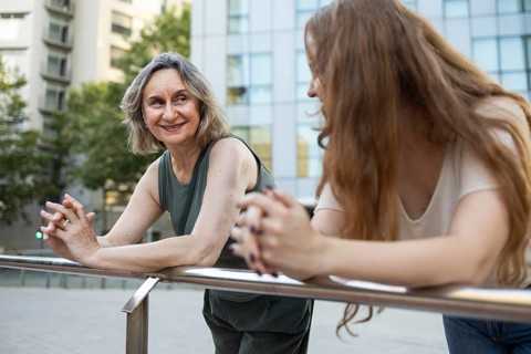 A joyful mother and daughter share quality time outdoors, leaning on a railing with a modern