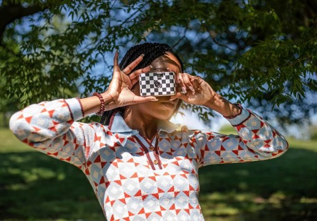 A woman is joyfully capturing photos in a lush, green natural setting under a vibrant blue sky. The