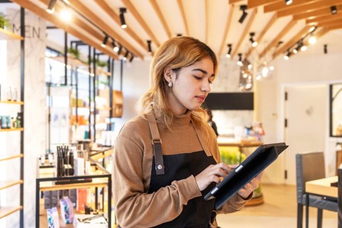 A cosmetics store worker uses a tablet in a well-lit, modern retail environment. The space features
