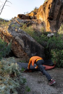 An adventurous climber gears up to tackle a challenging boulder in a picturesque natural setting.