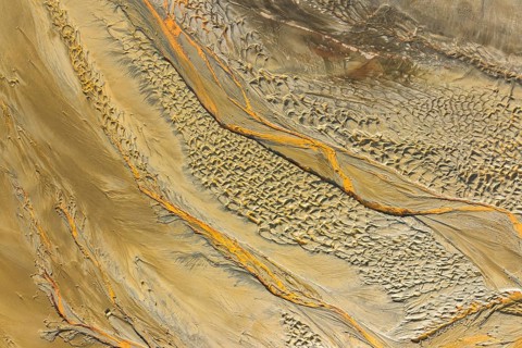 Aerial view captures a textured sand scape, showcasing flowing patterns of earthy tones and