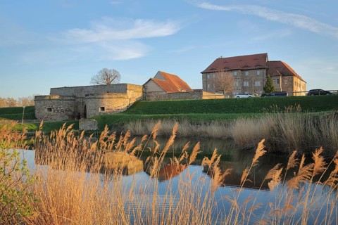 Renaissance moated castle with pond and reed grass on the shore, reflection, lighting mood,