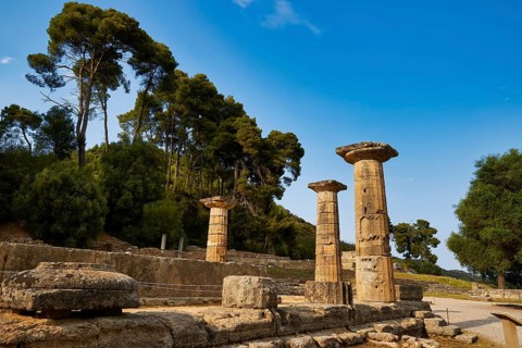Hera Temple, Heraion, stone pillars against a background of tall trees and bright blue sky,