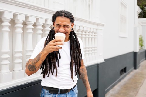 A cheerful man with dreadlocks and tattoos enjoys a coffee in Barranco, Lima, Peru He stands