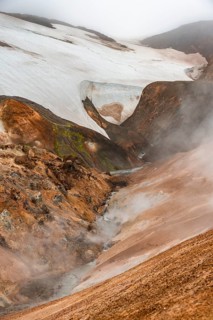 Steaming stream between colourful rhyolite mountains and snowfields, Hveradalir geothermal area,