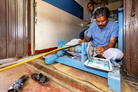 A man works concentratedly with a machine sitting on the floor, in a small room, The gemstone