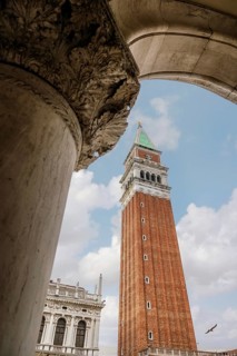 A stunning perspective of St. Mark's Campanile in Venice, framed by an ornate stone archway. The