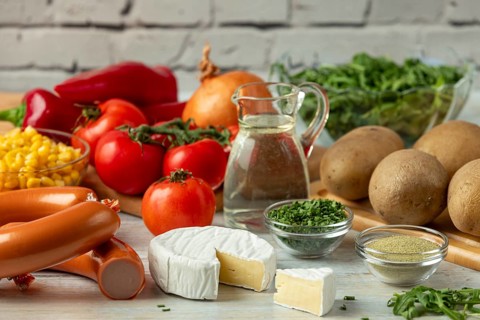 Fresh ingredients such as potatoes, tomatoes, peppers, sausage, corn, onions, cheese and arugula in