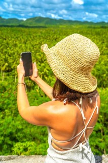 Young woman wearing a straw hat taking pictures of a coconut plantation in siargao island,