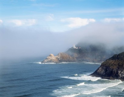A scenic coastline featuring a lighthouse emerging from the mist atop rocky cliffs, surrounded by