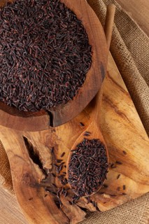 Natural black rice in a wooden bowl and spoon on a wooden surface in rustic style, top view