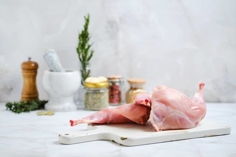 Raw rabbit hind legs on a cutting board, ready for stew preparation. Close by are herbs, spices,
