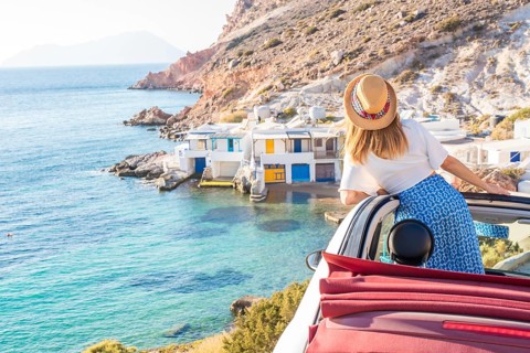 A woman in a convertible enjoys the stunning view of Fourkovouni, Milos Island. The vibrant