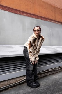 Stylish woman poses against an urban backdrop, showcasing a faux fur jacket, wide pants, and