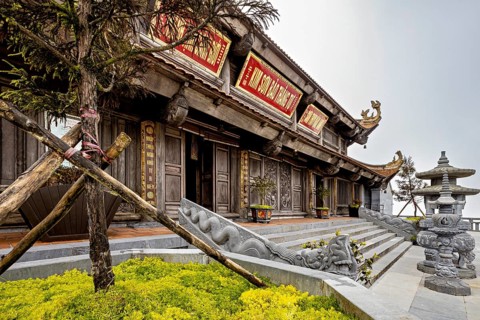Traditional temple with wooden façade, surrounded by stone sculptures and plants, The temple