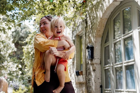 A joyful mother holding her cheerful daughter as they enjoy a sunny day outside. The scene captures