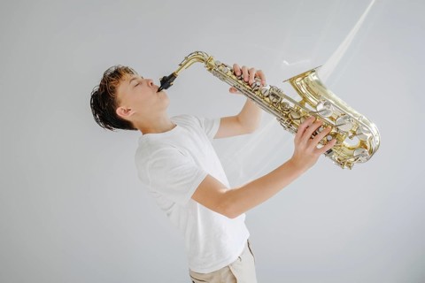 A young musician passionately playing a saxophone, dressed in a white shirt against a simple