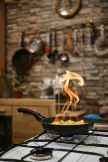 Flames are dancing from a skillet on the stove as vegetables are being sauteed in a cozy kitchen.