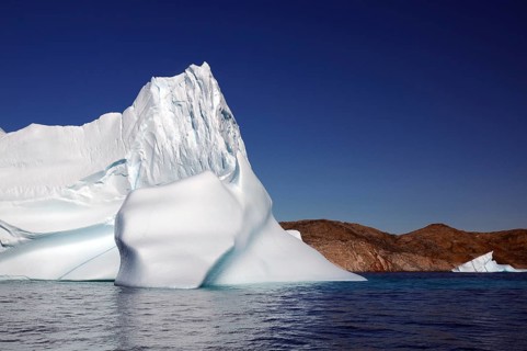 An imposing iceberg in clear blue water under a cloudless sky, Tasilaq, Arctic, Greenland, Denmark