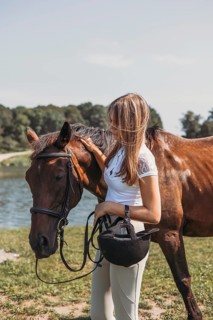 A young girl stands with her horse near a scenic lake. She gently pats the horse, creating a
