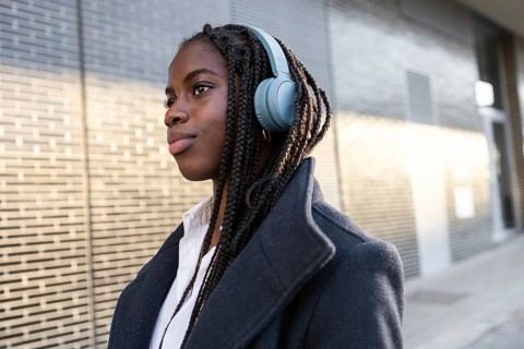 African American businesswoman with braids takes a break outdoors, wearing headphones and looking
