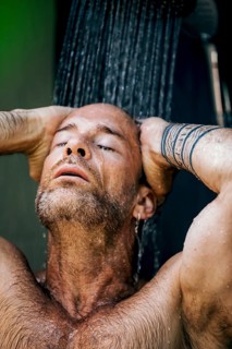 A man enjoys a relaxing moment under a refreshing shower, feeling the water cascading over him. The