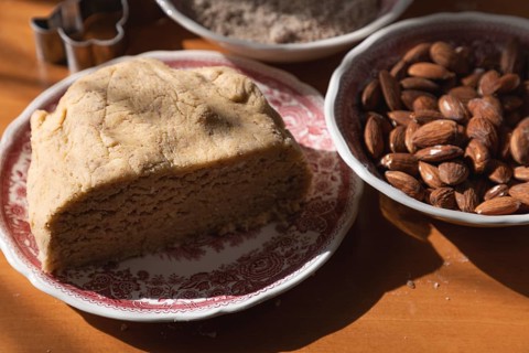 Small lump of dough on a plate next to almonds in a bowl of flour