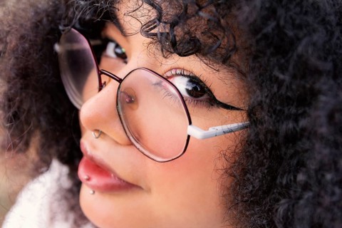 Close-up view of a latin woman wearing round glasses and showcasing curly hair. Her captivating