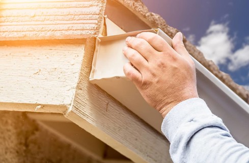 Worker Attaching Aluminum Rain Gutter to Fascia of House
