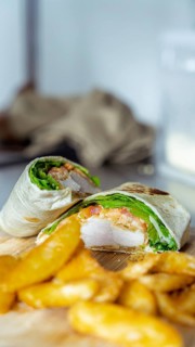 A close-up of a mouthwatering chicken wrap, filled with fresh lettuce and tomato, accompanied by