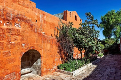 Sun-drenched walkway with vivid orange walls and lush plants, Santa Catalina Monastery in Arequipa