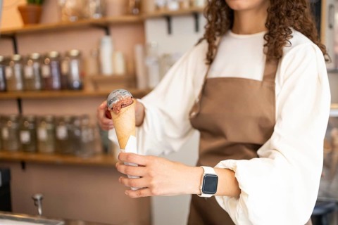 A woman clerk in a stylish brown apron serves a delicious ice cream cone in a cozy shop. The