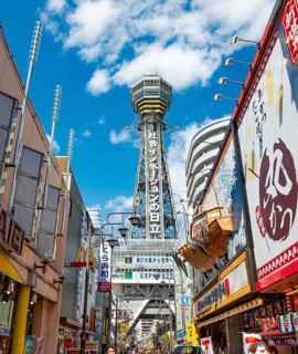 Lots of colorful signs in a pedestrian zone with shops and restaurants, behind Tsutenkaku Tower,