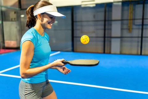 Young woman playing pickleball, smiling and holding a paddle while looking at the ball during a