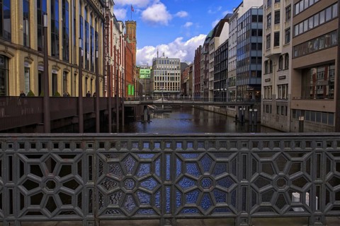 Decorative bridge with a view of a canal between tall buildings under a blue sky, Hamburg, Germany