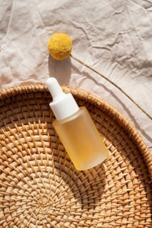 A minimalist flat lay of a cosmetic containing skincare oil, placed on a woven mat alongside a